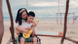 Asian disabled teenager boy on wheelchair and mother playing ukulele happily on the beach, Lifestyle of happy handicapped teen travel activities in beautiful nature background, Mental healthy concept.