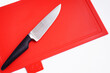Bright red clean plastic cutting board with a kitchen knife on a white background.