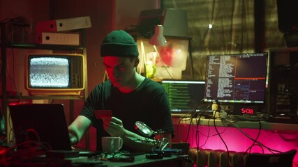 Young hacker breaking password of credit bank card. Man programmer infecting system with cyber virus, stealing money, using laptop computer, developing program in dark room. 