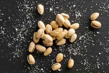 Wall Mural - Heap of salted, roasted green pistachio nuts snack on black background with sea salt, healthy food snack