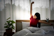 © Anatta_Tan - Asian attractive woman is sitting on a clean white bed, stretching her arms to muscle relaxation After she woke up, concept to The pleasure of resting with deep sleep on a soft and clean bed.