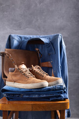 Wall Mural - Denim jeans and old boots at chair. Stack of jeans near abstract background