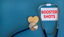 Covid-19 Booster Shots Vaccine Symbol. White Card With Words Booster Shots, Beautiful Blue Background, Wooden Heart And Stethoscope. Covid-19 Booster Shots Vaccine Concept.