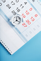 Wall Mural - Time on a white alarm clock lying on the calendar and a blue background.