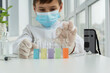 © Anna - Young scientist in protective clothers is preparing to pick one of test tubes with liquids of different colors, scientific experiments.