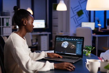 Wall Mural - Focused african american engineer woman working at industrial gear prototype late at night in startup business company office. Engineering product construction idea on laptop screen