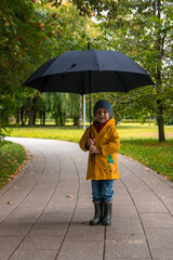 A boy walking under an umbrella in a yellow raincoat. Cloudy weather