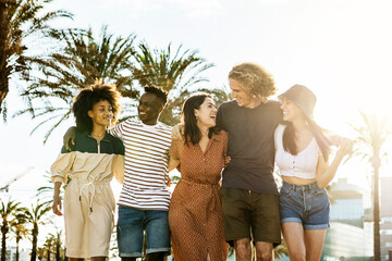 Millennial group of friends walking embraced while laughing outdoors in summer - Happy young people celebrating together while talking in the beach - Unity and youth lifestyle concept