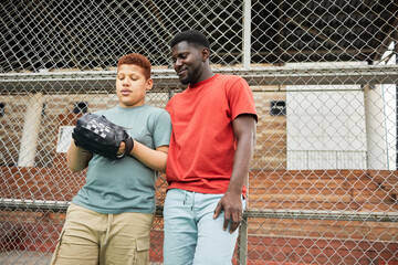 Smiling African-American embracing teenage son in baseball mitt while visiting baseball training with him