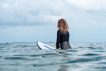 Portrait of surfer girl on white surf board in blue ocean pictured from the water