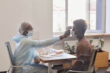 Wall Mural - Doctor using digital non-contact infrared thermometer to measure temperature of patient before giving vaccine against coronavirus