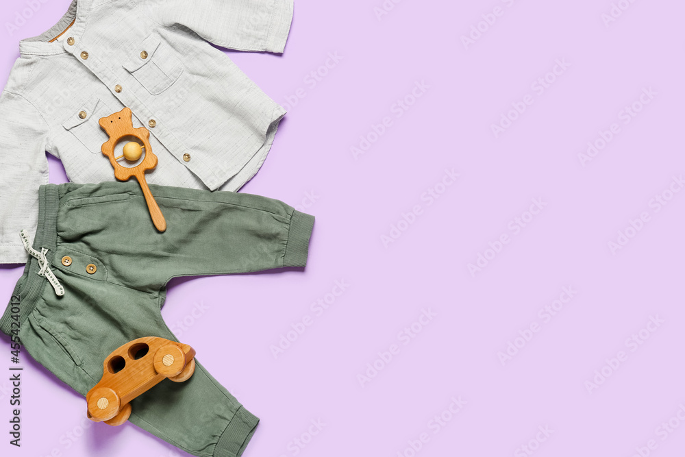 Stylish baby clothes with toys on color background