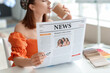 © Pixel-Shot - Young woman drinking coffee while reading newspaper at home