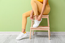 Woman In Stylish Shoes Sitting On Stool Near Color Wall