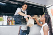 Smiling salesman giving packages with street food to a female customer. Food truck owner serves the buyer.