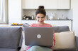 © deniskomarov - Smiling caucasian girl student professional employee working on laptop sitting on sofa at home office. Happy female studying online, using apps for work, e-learning and education concept.