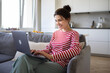 © deniskomarov - Smiling  girl freelancer using laptop studying online working from home office. Happy millennial woman typing on pc surfing internet looking at screen enjoying distant job sitting at sofa.