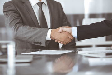 Unknown business people are shaking hands after contract signing in modern office, close-up. Handshake as successful negotiation ending