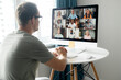 © Vadim Pastuh - Morning meeting on the distance. Back view over shoulder of guy to the computer screen with a lot of diverse people on it, work team brainstorming, discussing together, virtual meeting colleagues