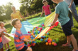 © New Africa - Group of children and teacher playing with rainbow playground parachute on green grass. Summer camp activity