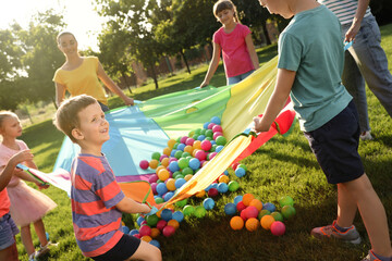 Wall Mural - Group of children and teacher playing with rainbow playground parachute on green grass. Summer camp activity