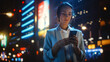 © Gorodenkoff - Beautiful Young Woman Using Smartphone Standing on the Night City Street Full of Neon Light. Portrait of Young Woman Holding Mobile Phone, Posting Social Media, Online Shopping, Texting.