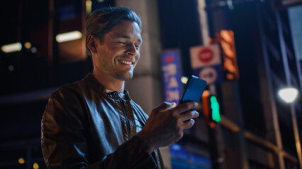 Sticker - Portrait of Handsome Young Man Using Smartphone Standing in the Night City Street Full of Neon Lights. Smiling Stylish Blonde Male Using Mobile Phone for Social Media Posting.