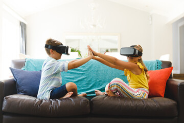 Wall Mural - Caucasian brother and sister sitting on couch and using vr headsets in living room