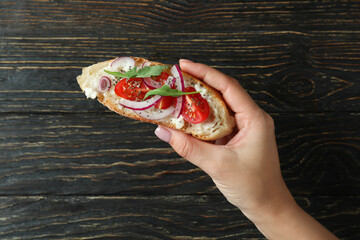 Female hand holds bruschetta on rustic wooden background