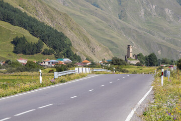 Poster - Closeup shot of an asphalt road in mountainous landscape with a village in the background