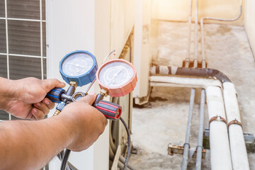 Air repair mechanic using measuring equipment for filling industrial factory air conditioners.	