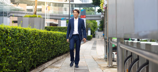 Wall Mural - Asian businessman wearing suit jacket walking go to work in morning outdoor.