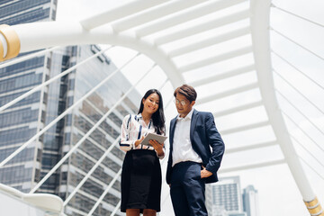 Asian business man talking on mobile phone and young beautiful woman working on digital tablet computer standing outside office building.