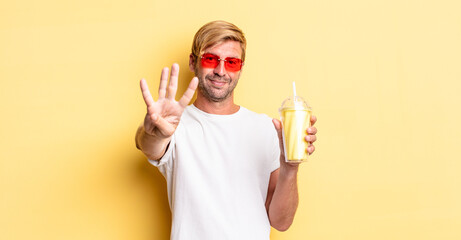 Wall Mural - blond adult man smiling and looking friendly, showing number four with a milkshake