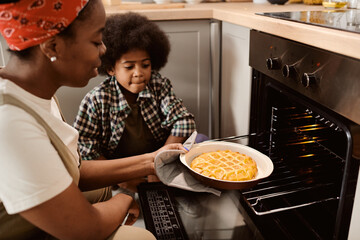 Cute boy looking at fresh hot apple by held by his mom over bars of electric oven