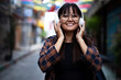 © JustLife - Young smiling woman outdoors. Beautiful woman listening to music while walking through the city