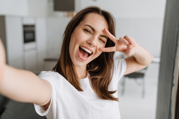 Wall Mural - Young white woman smiling and gesturing while taking selfie photo