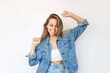 © Марина Демешко - A young pretty caucasian excited smiling blonde woman in a denim jacket and jeans is happy about the news or lottery win isolated on a white background. Cheerful girl dances with her hands up