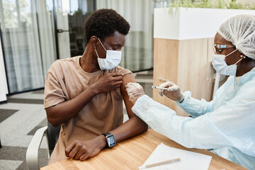 Wall Mural - Young African American man sitting at doctors office and getting flu shot in his arm