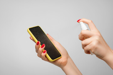 Woman's hands spray disinfectant on mobile phone to clean and protect against viruses. Cleaning smartphone by alcohol hand sanitizer.