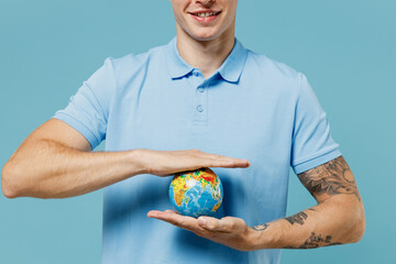 Close up cropped young curly man 20s years old wear azure t-shirt hold in palms Earth world globe isolated plain pastel light blue background studio portrait. Ecology environment protection concept