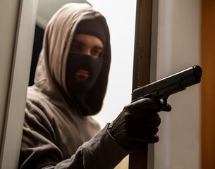 Wall Mural - Criminal with balaclava holds gun in leather gloved hand behind door. Terrorism, violence