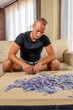 © Andres - Attractive teenage man in a black t-shirt assembling a puzzle in the living room at home. Training concept