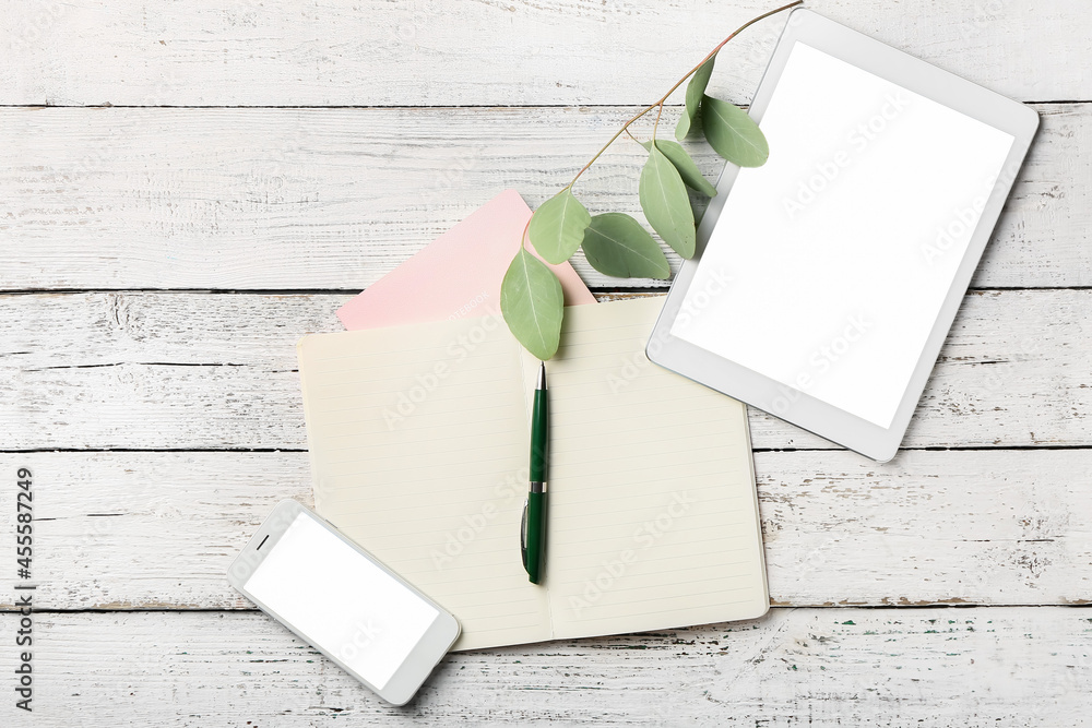 Notebooks, mobile phone, tablet computer and pen on light wooden background