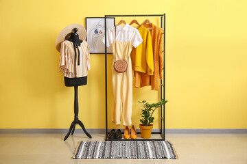 Rack with stylish clothes, shoes and accessories near color wall