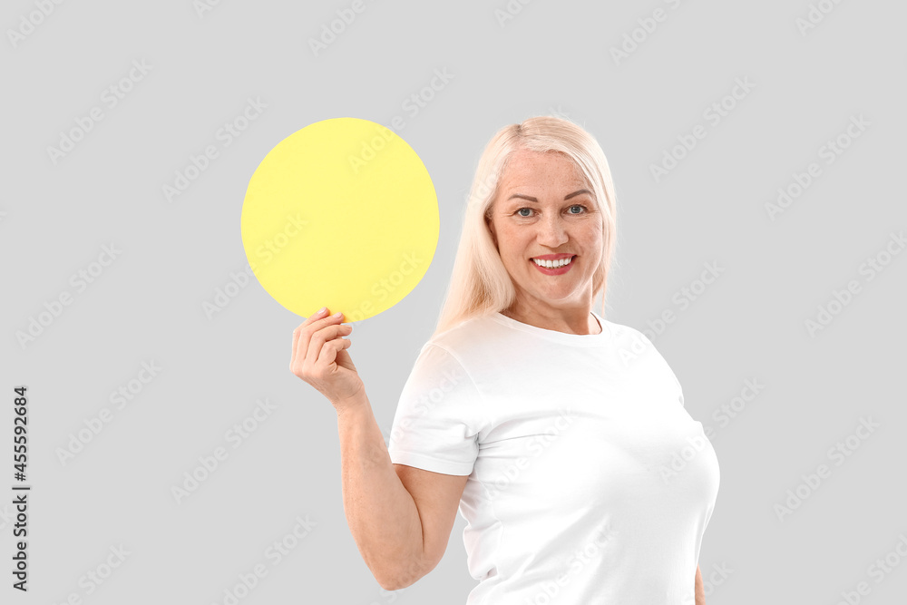 Mature woman with blank paper sheet on light background