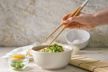 Woman eating tasty Chinese soup with chicken on light background, closeup