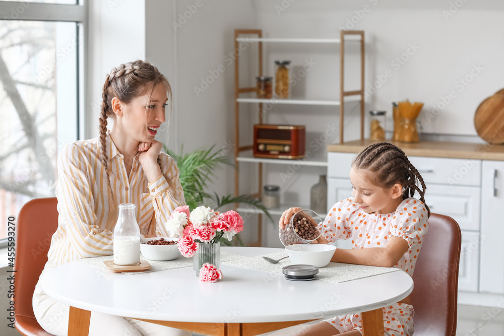 Little girl and her mother having breakfast in kitchen