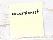 Yellow sticky note on wooden wall with handwritten word excursionist