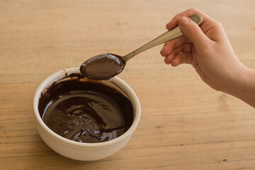 Sticker - Shot of a hand taking melted chocolate with a spoon from a white ceramic bowl on a wooden table